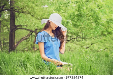 Beautiful woman in a hat with wide brim reads a book in summer park