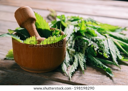 Leaves of nettle in mortar with pestle on wooden background, medicinal herb