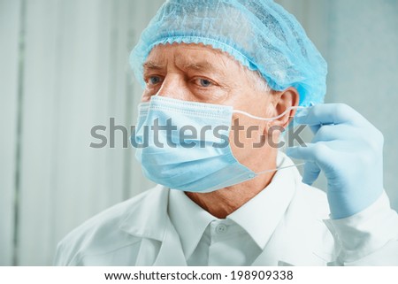 Senior man surgeon takes off his protective mask after operation