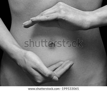 Unrecognizable woman holds her hands in circle shape in front of her abdomen, monochrome image