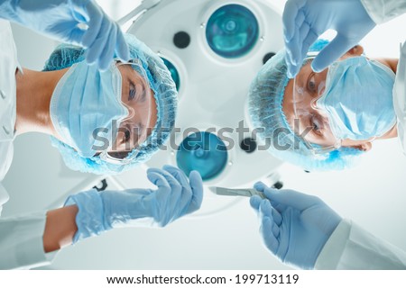 Woman nurse assistant passes a scalpel to man surgeon on operation on background of surgical lamp. Focus on the woman nurse