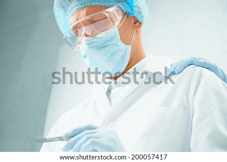 Serious man surgeon with scalpel on operation, hand on his shoulder, supporting gesture
