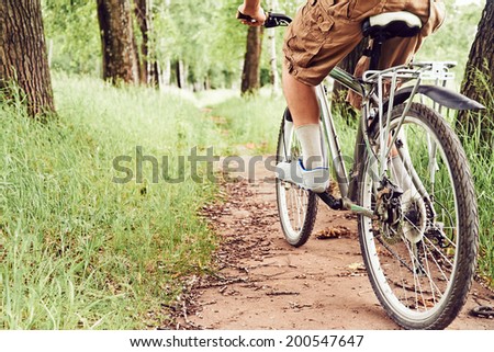 Man is riding bicycle on path in summer park, face is not visible