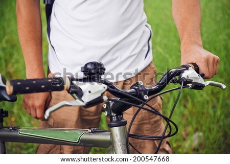 Close-up image of cyclist man hands holds handlebar of mountain bike in summer park, face is not visible