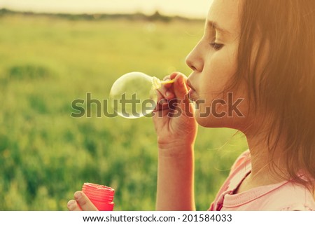 Little girl is blowing a soap bubbles in summer field, close-up portrait. With instagram filter