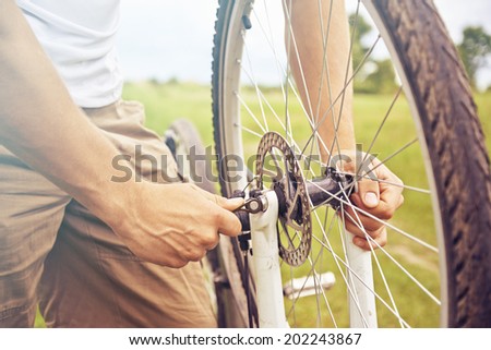 Cyclist man checks wheel of bicycle in summer park, face is not visible, repair of bicycle