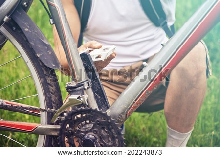 Close-up image of cyclist man checks pedal of bicycle in summer park, face is not visible