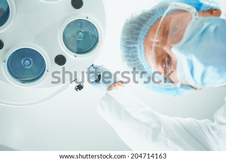 Assistant surgeon in protective uniform places a surgical lamp in operating room and looks at camera. Point of view shot