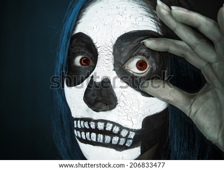 Young woman with dark Halloween skull makeup shows her scary eye