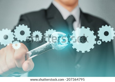 Businessman in a suit holds wrench with cogwheels, focus on wrench, concept of business creation