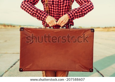 Woman holds brown vintage suitcase, face is not visible, copy-space