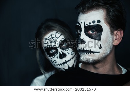 Couple with dark skull makeup on black background. Halloween face art