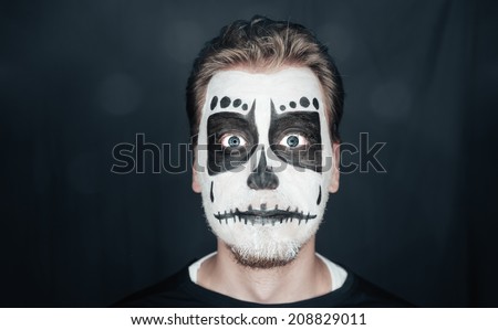 Portrait of surprised young man with skull makeup. Halloween face art
