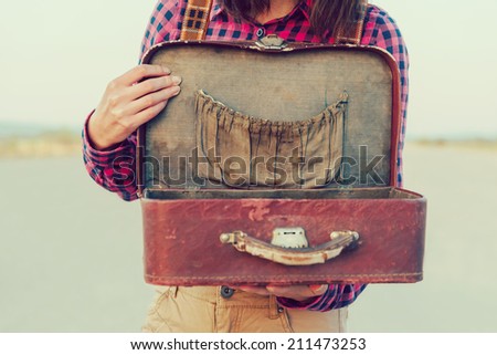 Unrecognizable traveler woman holding open vintage suitcase. With vintage filter