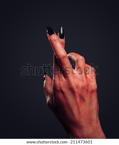 Red demon or devil hand with gesture cross fingers on dark background. Halloween/horror theme