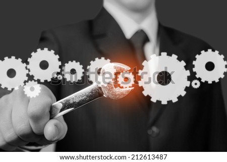 Businessman in a suit holds wrench with cogwheels, focus on wrench, concept of business creation. Monochrome image