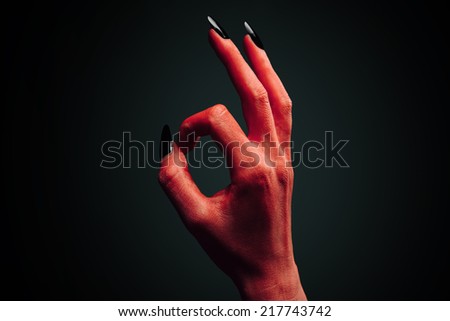 Red demon or devil hand with gesture OK on dark background. Halloween/horror theme