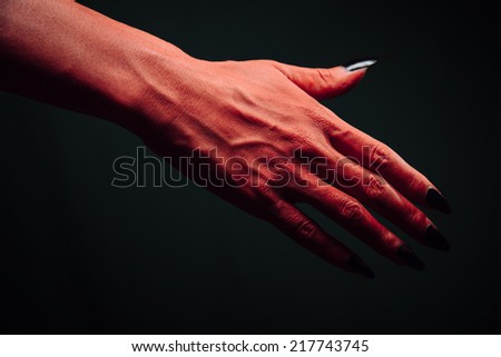 Red demon or devil hand with handshake gesture on dark background. Halloween or horror theme