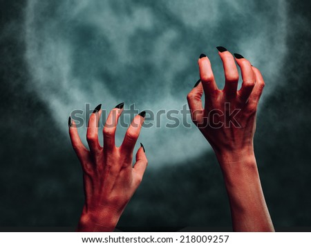 Red hands of the demon on background of full moon. Halloween or horror theme