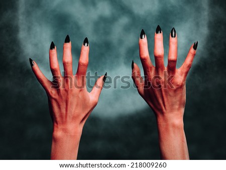 Red hands of the devil on background of full moon. Halloween or horror theme