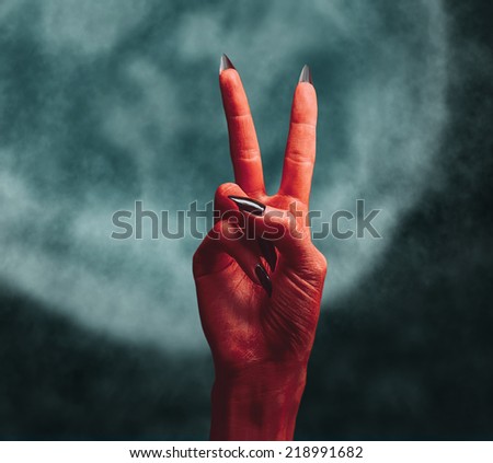 Red devil hand on dark background, peace hand sign. Halloween or horror theme
