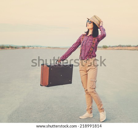 Happy traveler young woman with vintage suitcase walks on road, hipster style.