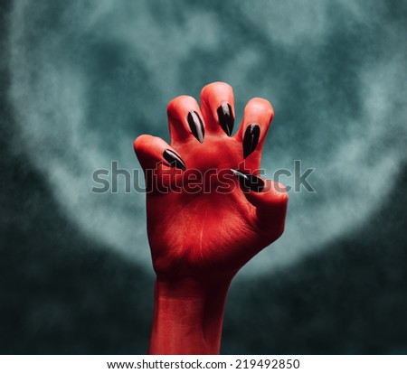 Scary red devil hand on background of full moon. Halloween or horror theme