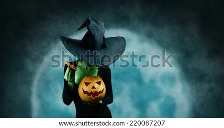 Green witch opening Halloween carved pumpkin on full moon background. Halloween, horror theme