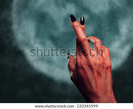 Red demon or devil hand with gesture cross fingers on background of full moon. Halloween/horror theme