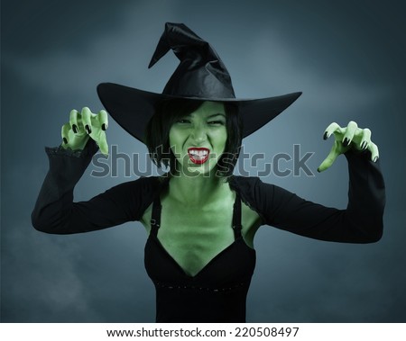 Scary witch with green skin performs magic on dark background. Halloween, horror theme.