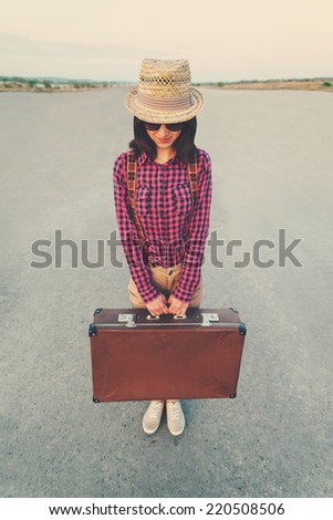 Traveler hipster girl stands on road with vintage suitcase