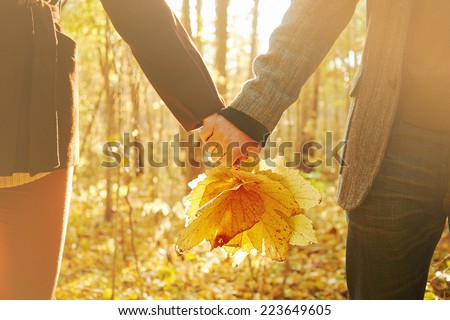 Young couple in love holding hands with leaves in autumn park, face is not visible