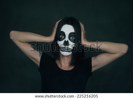 Woman with Halloween skull makeup holding her head with fear emotions