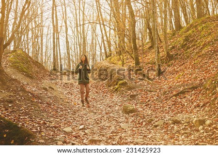 Smiling hiker woman walking in beautiful autumn forest, dry yellow leaves on land. Hiking and leisure theme. Image with sunlight effect