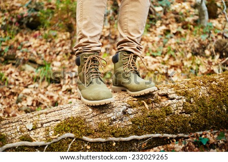 Hiker woman standing  on fallen tree trunk in autumn forest, view of legs. Hiking and leisure theme