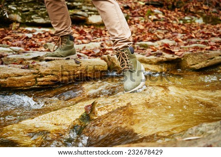 Hiker woman crossing a stream in autumn forest, view of legs. Hiking and leisure theme