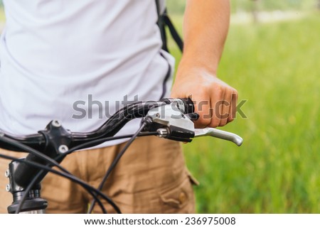 Cyclist male hand holding handlebar of mountain bike in summer park, close-up image, face is not visible