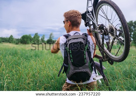 Cyclist man with backpack carries bicycle in green meadow in summer. Theme of sport and hiking