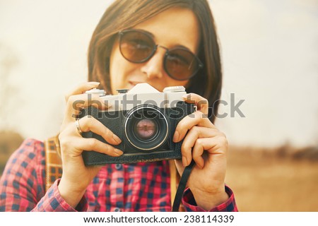 Traveler smiling young woman takes photographs with vintage old photo camera in spring outdoor. Focus on photo camera