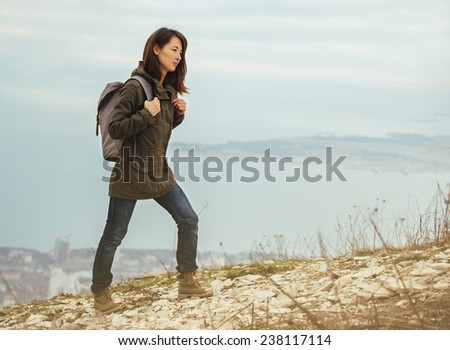 Young hiker woman with backpack walking in highlands on background of sea. Hiking and recreation theme
