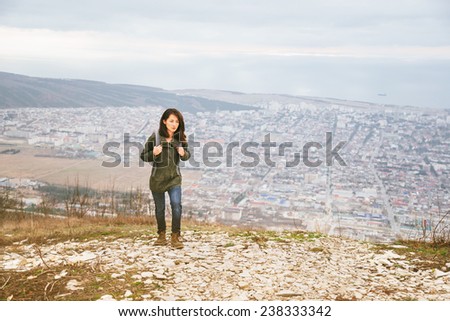 Young hiker woman with backpack walking in highlands over the city. Hiking and recreation theme