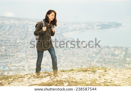 Young traveler woman with backpack walking in highlands over the city. Hiking and recreation theme
