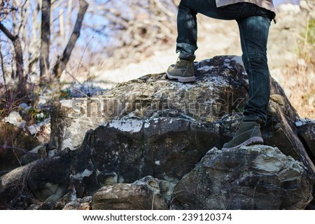 Unrecognizable hiker woman go up on rock, view of legs. Hiking and recreation theme