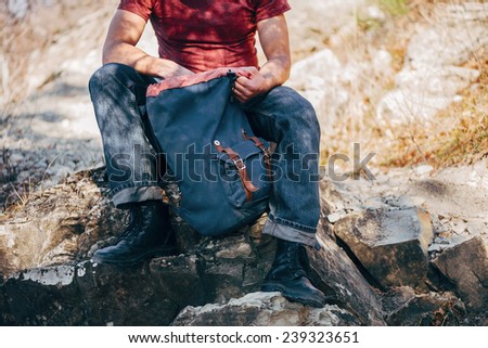 Unrecognizable hiker man looking for something in backpack on nature. Hiking and recreation theme