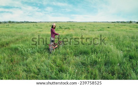 Young woman in straw hat walking with bicycle on summer meadow outdoor