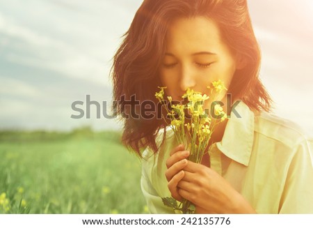 Beautiful young woman smelling yellow flowers with closed eyes in summer outdoor. Image with sunlight effect