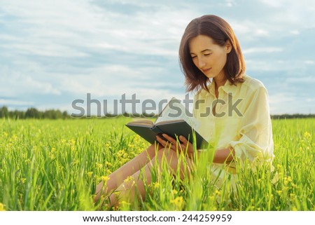 Smiling beautiful girl reading a book on summer meadow