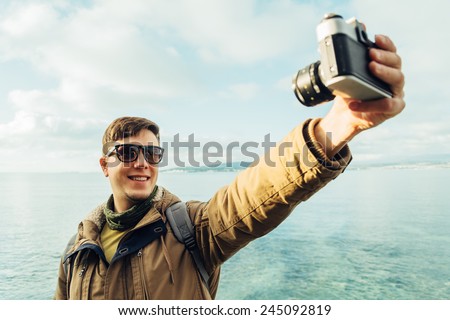 Traveler happy young man takes photographs self portrait with old photo camera on coastline on background of sea