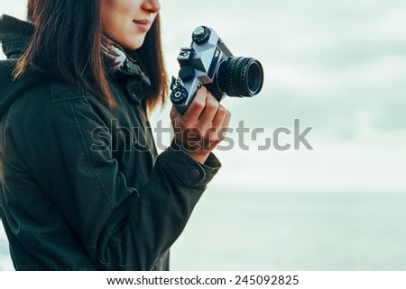 Smiling young woman holding vintage old photo camera on background of sea. Concept of travel and hiking