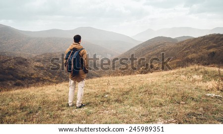 Hiker man with backpack standing on hill and enjoying by scenic of mountains, rear view